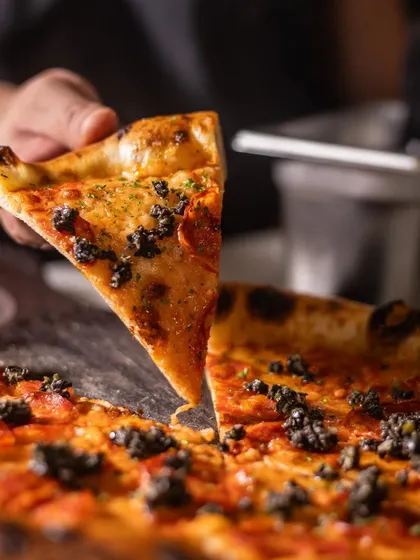 Slice, slice, baby. A single slice of pepperoni and olive tapenade pizza is held up, ready to be enjoyed. It's the perfect bite.