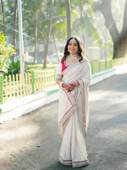 A full-length shot of the bride in an elegant white saree, taking a stroll on a sunlit path. She looks serene, happy, and incredibly graceful.