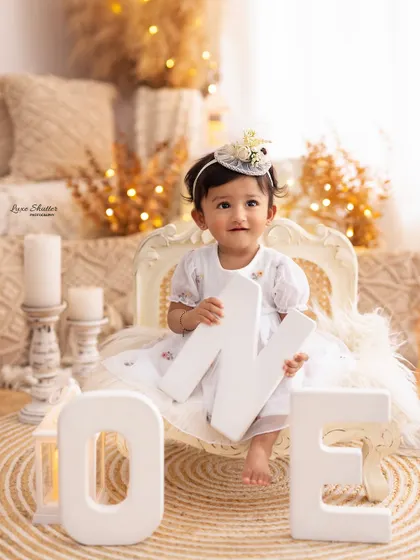 This little one is celebrating her first birthday, holding the letter 'N' from the 'ONE' sign in a stylish and warm boho-themed setting.