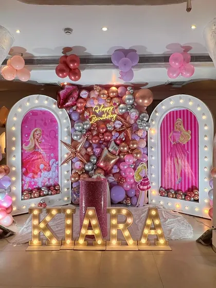 A glamorous Barbie themed birthday stage with light-up arched panels, a metallic balloon backdrop, and marquee letters.