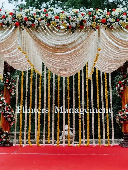 A traditional South Indian mandap, beautifully decorated with intricate drapes of jasmine and marigold flowers, creating a classic and divine atmosphere for the wedding rituals.