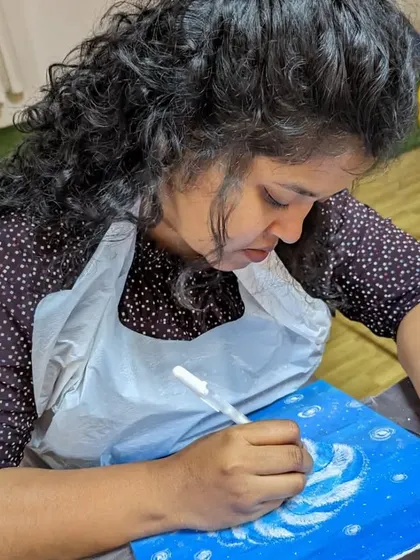 A participant adding details to her galaxy-inspired abstract painting. The swirling colors and white specks create a beautiful cosmic effect.
