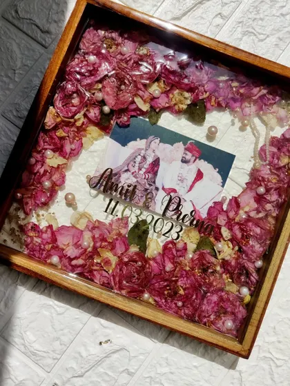 Your wedding varmala is a precious keepsake that deserves to be cherished. This finished teakwood frame, filled with pink roses and pearls, is a beautiful way to honor your special day.