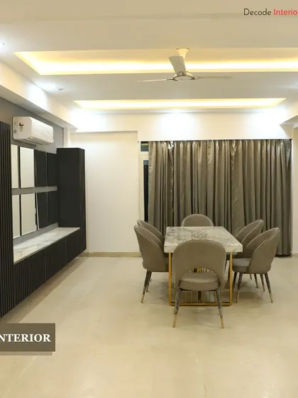 This dining area is designed for modern elegance. It features a marble-topped dining table with gold-finished legs, comfortable upholstered chairs, and a sleek, wall-mounted crockery unit.