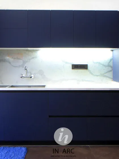"Everything happens in the kitchen. Life happens in the kitchen." This is a detail of a minimalist kitchen with deep blue cabinetry and a clean, white marble backsplash.