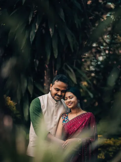 A loving couple framed by lush green foliage in a park. This style of portrait uses natural surroundings to create a sense of intimacy and seclusion.