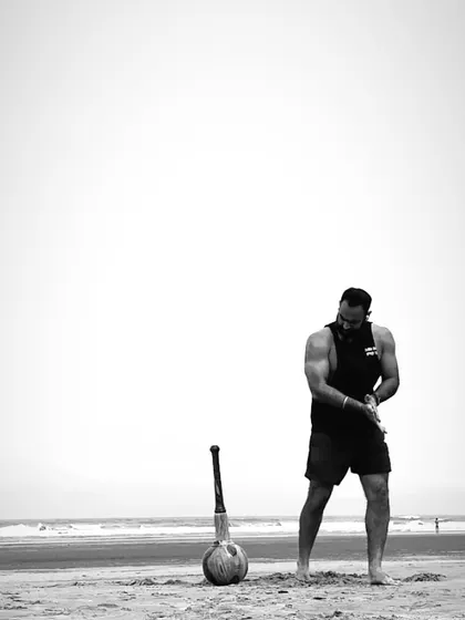 We didn't invent this; we just refused to forget it. Our founder stands with a Gada on a beach, a powerful image representing the timeless, pure, and demanding nature of this training system, born long before fitness was built in a room.