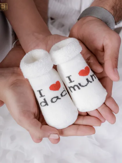 A close-up detail shot of parents holding a pair of tiny socks that say "I love mum" and "I love dad," a sweet announcement.
