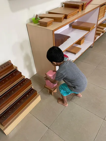 A child works with the Pink Tower, a classic sensorial material. This activity helps them visually discriminate between sizes and builds their understanding of dimensions, which is an indirect preparation for mathematics.