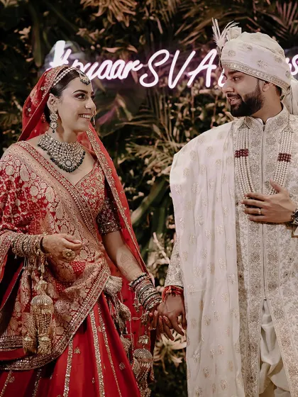 A beautiful candid moment between the couple, holding hands in front of their wedding hashtag.