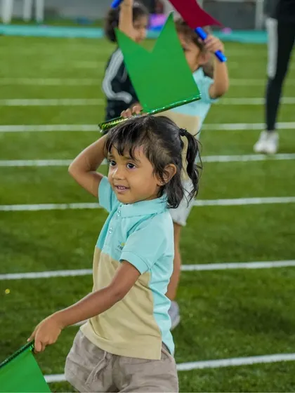 A child waves flags during a Sports Day drill, her face alight with joy and concentration.