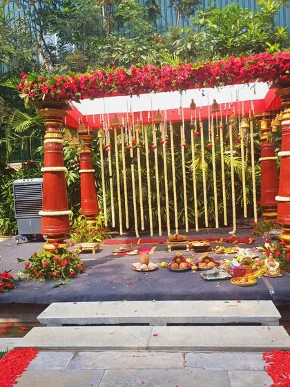 A beautiful outdoor mandap with red pillars and hanging bells, ready for a traditional Hindu wedding.