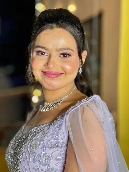 A happy client showing off her finished party look. The makeup is shimmery and glamorous, with a pop of purple on the eyes.