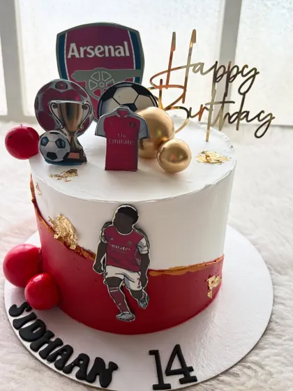 A cake for a true Arsenal fan. The design includes the team's logo, jersey, and a trophy, all in the classic red and white colors.