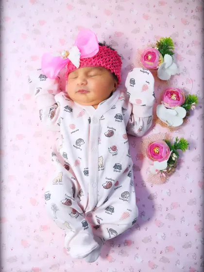 A peaceful baby girl in a pink knitted headband and a cute printed onesie, sleeping soundly.
