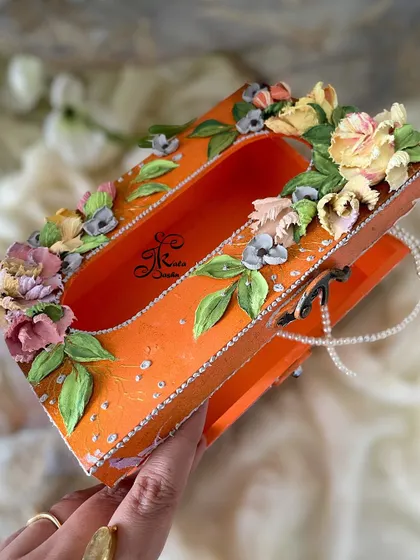 An angled view of the orange tissue box, revealing the pearl necklace detail inside.