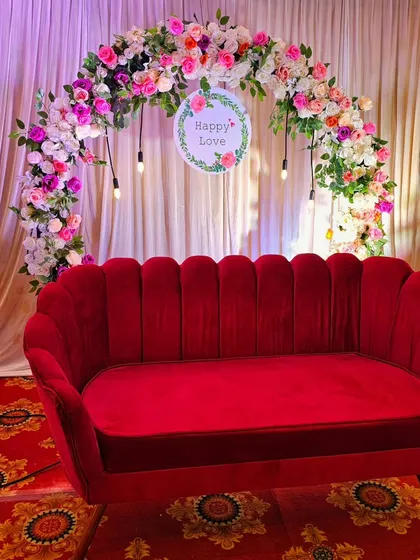 A romantic "Happy Love" setup, perfect for an anniversary or engagement party. The floral arch and plush red velvet sofa create an elegant and inviting photo spot.