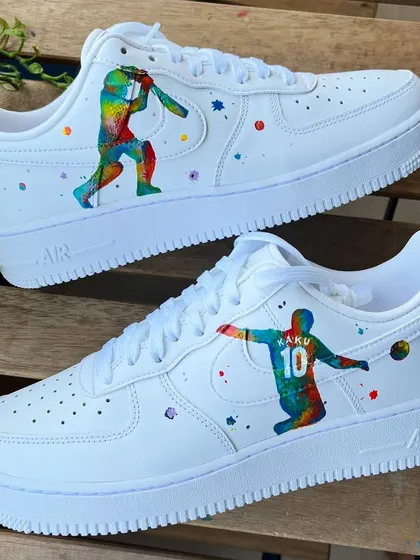 A vibrant, abstract take on sports. These custom Nike AF1s feature colorful silhouettes of a cricketer and a football player, surrounded by paint splatters.