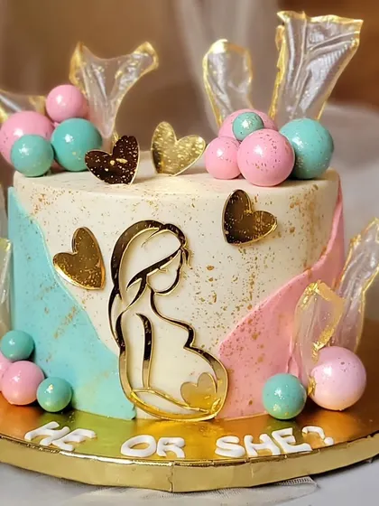 A beautiful "He or She?" gender reveal cake. The pink and blue watercolor effect, gold hearts, and rice paper sails create a modern and elegant design.