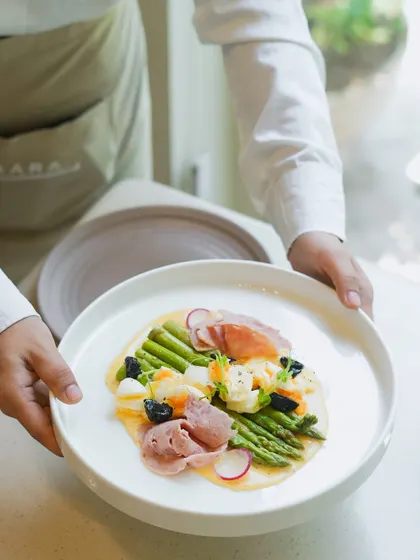Our chef presents a signature summer dish featuring Himalayan asparagus. This plate highlights our philosophy of using the freshest seasonal produce, served with traditional hollandaise sauce and prosciutto for an elegant dining experience.