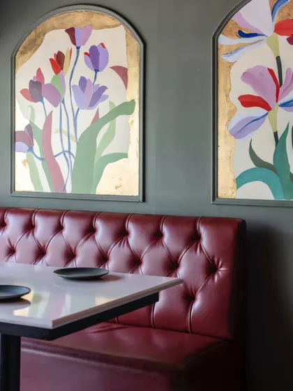 Two arched floral murals seen in their restaurant setting, complementing the rich red of the tufted leather booth. The gold leaf catches the light, creating a warm and inviting atmosphere.