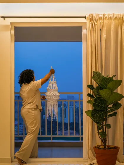 This image captures the transition from a warm, curated interior to the cool evening cityscape. The design balances contrast and harmony, using soft lighting, a lush fig plant, and a large balcony door to frame the view and invite the urban skyline indoors.