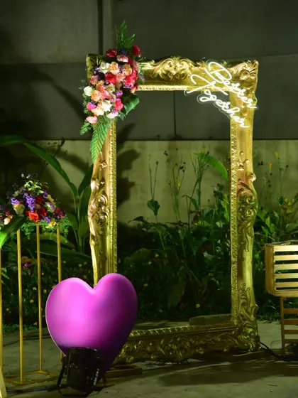 A creative photo booth for a reception, using a large ornate golden frame and neon signs.