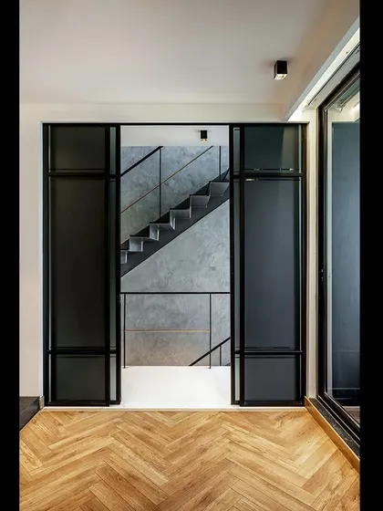A framed view of the steel staircase in the SOL House, seen through an interior glass partition. This composition highlights the clean lines and industrial aesthetic that define the project's interior design language.