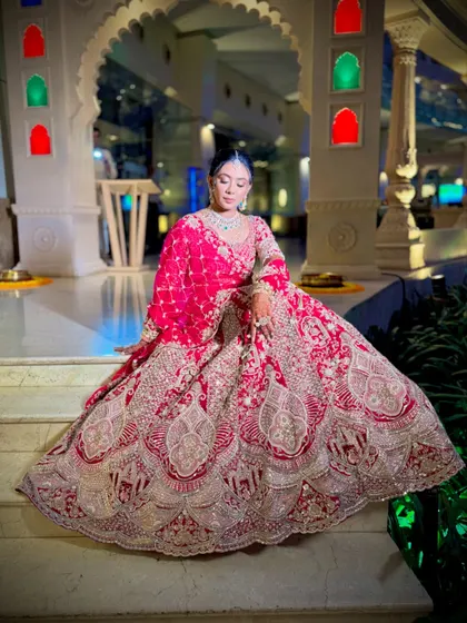 A royal portrait of the bride seated on steps, her elaborate red and silver lehenga spread out beautifully.