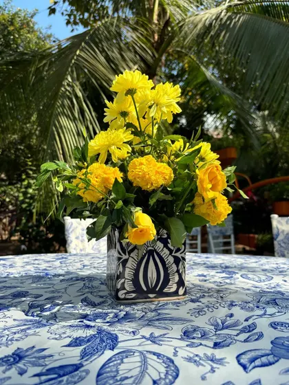 Another elegant centerpiece, combining a square blue and white vase with yellow blooms on a printed tablecloth.