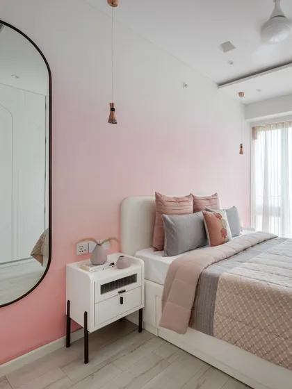 Welcome to a dreamy pink bedroom featuring ombré spray-painted walls. The room includes a compact study area with fluted panels and sliding wardrobes with back-painted glass for a touch of refined opulence.