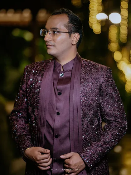 A handsome portrait of the groom in his intricately embroidered maroon reception outfit, against a bokeh background.