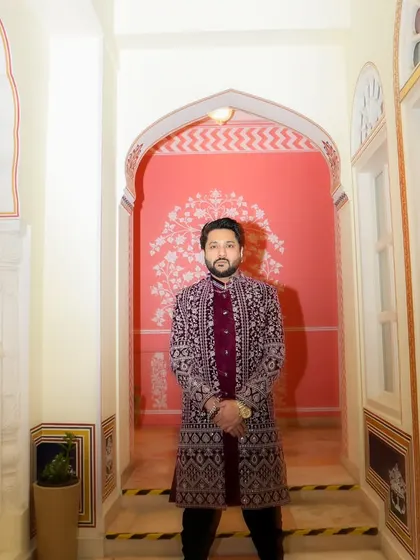 A portrait in a royal maroon sherwani, standing in a beautifully arched hallway. This look is perfect for a grand, traditional Sufi night.