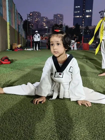 Anika holds her split, showing incredible progress and determination. This level of flexibility is achieved through consistent practice and is essential for advanced Taekwondo kicks.