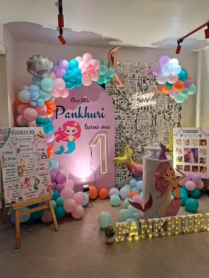 Pankhuri's first birthday was a mermaid adventure! This setup features a custom arched backdrop, a milestone board, and a beautiful pastel balloon garland with a neon "Happy Birthday" sign.