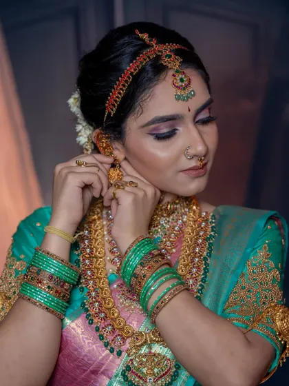 A close-up of the model adjusting her earring, giving a clear view of the jhumka and the matha patti.