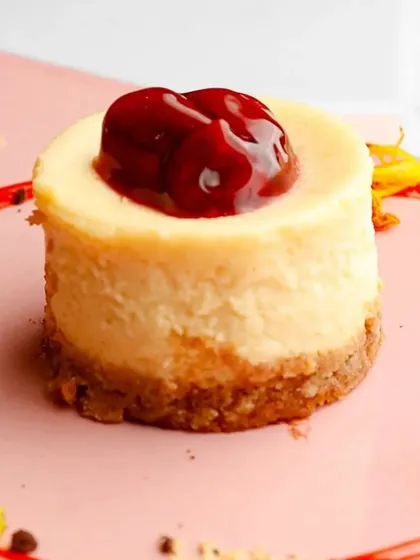 A perfectly formed individual Baked Cherry Cheesecake. The glossy cherry topping contrasts beautifully with the creamy, pale filling and the golden-brown biscuit base.