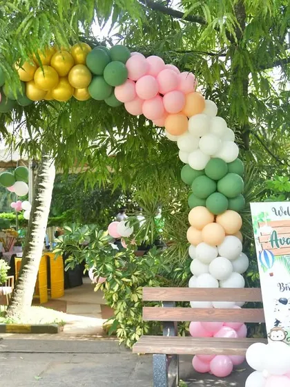 This outdoor jungle-themed entrance features a pastel balloon arch that complements the natural greenery. A bench and a welcome sign create a perfect spot for guests to take photos as they arrive.