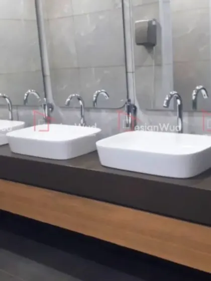 A view of a modern office washroom we designed, focusing on hygiene and durability. The space features multiple vessel sinks on a dark, solid countertop with a wood-laminate base, complemented by large mirrors and easy-to-clean wall tiles. This demonstrates our comprehensive approach to commercial interior projects.