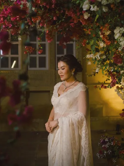 The bride, framed by an arch of vibrant bougainvillea, looks serene and beautiful in her elegant white saree.
