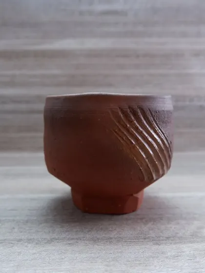 A Japanese-style earthenware tea bowl, or chawan. The carved lines on the side give it a modern feel, while the faceted base provides a comfortable grip. It's designed for the quiet ritual of tea.