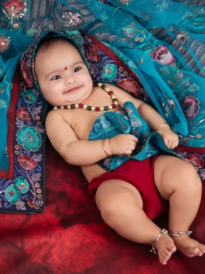 A playful and chubby 6-month-old dressed in a traditional style, showing off a heart-melting smile.