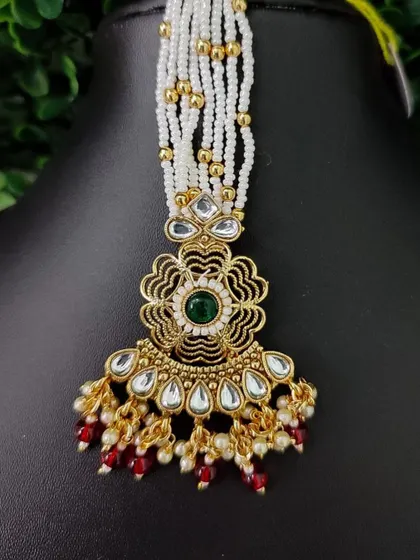 This maang tikka features a floral pendant with a central green stone, attached to strands of white pearls. It’s a beautiful blend of traditional and contemporary design.
