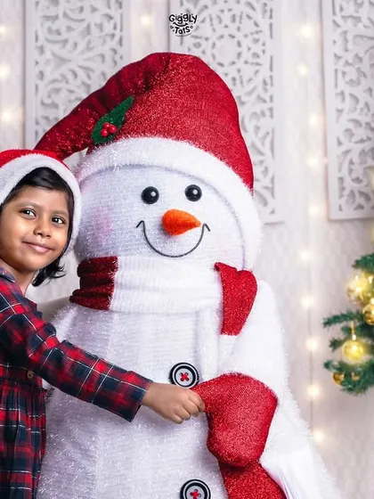 A young girl shares a happy hug with our friendly studio snowman, her smile as bright as the Christmas tree beside them.