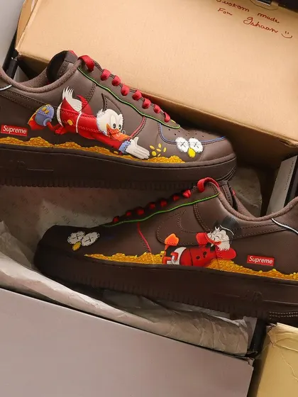 This design is a mashup of two iconic art styles. I hand-painted Kaws-inspired elements alongside the classic cartoon character Scrooge McDuck on a pair of brown Nike Air Force 1 Supreme lows.