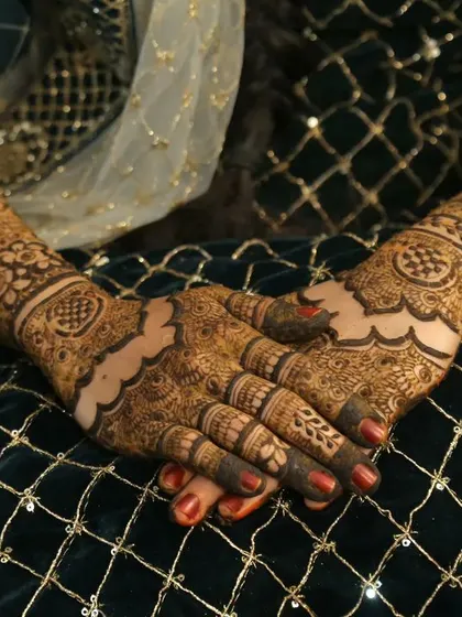 A beautifully composed shot of a bride's hands, showcasing the detailed henna work against her elegant dark green and gold outfit.