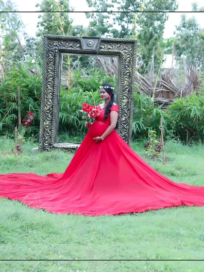 A dramatic wide shot of a red maternity trail gown, spread out across a lush green lawn.