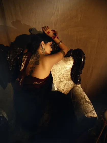 A back profile shot that focuses on the model's tattoo and the beautiful texture of the saree, all under soft, moody lighting.