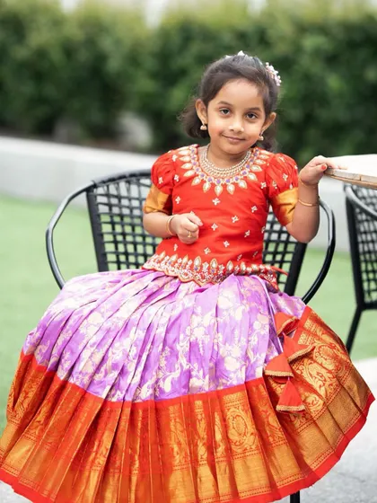 This little one looks so sweet in her custom Kanchi Pattu lehenga. The red embroidered blouse and the pleated lavender silk skirt with a wide orange and gold zari border is a classic and colorful combination.