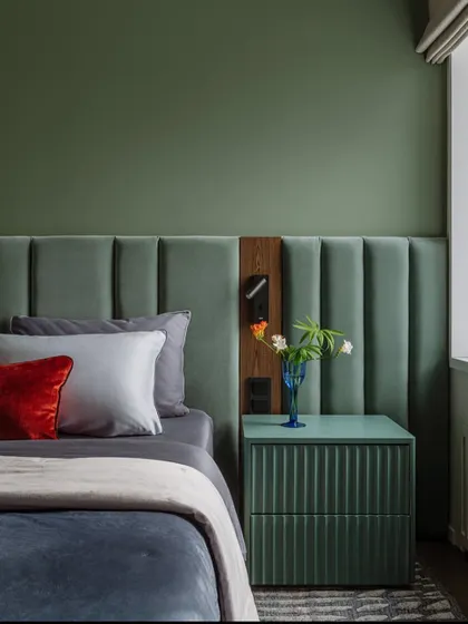 The right color can make all the difference. This bedroom uses a soothing green for the wall and headboard, creating a calm and relaxing environment. The fluted bedside table adds a touch of modern texture.